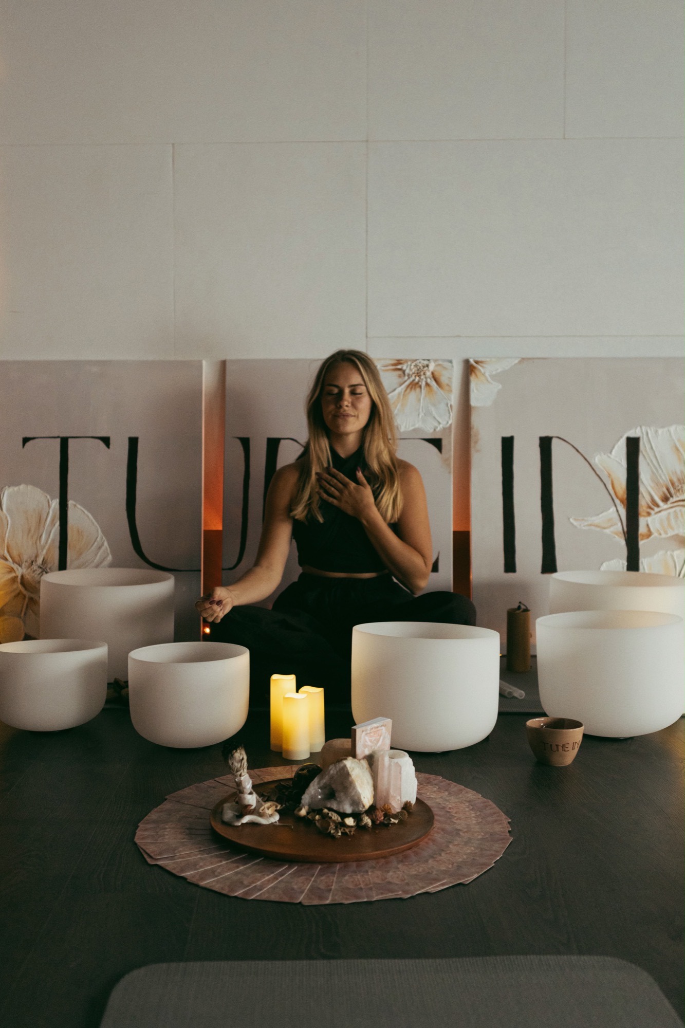Sem seated cross-legged with a hand on her heart, surrounded by crystal singing bowls